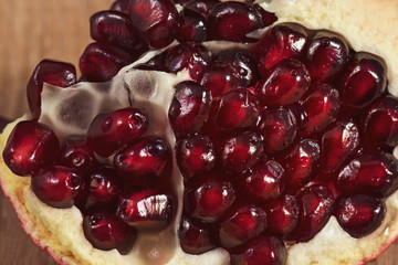 Close-up: A slice of peeled pomegranate lies on a light wood kitchen board. Bright red grains of...