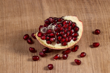 A slice of peeled pomegranate lies on a light wood kitchen board, juicy bright grains of pomegranate are scattered on the surface. Photo under artificial lighting with two light sources.