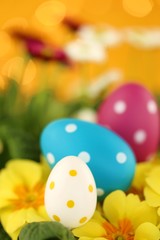 Obraz na płótnie Canvas Easter holiday.Easter eggs and spring flowers. Decorative eggs set on yellow primrose flowers on bright orange with bokeh background.Spring festive background.