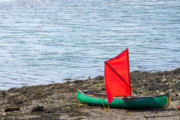 Green canoe with red sail on sandy beach