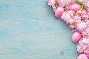 Pink flowers end eggs are on blue wooden background