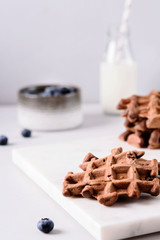 Homemade Chocolate waffles, milk and blueberries on white marble tray. Breakfast. Selective focus