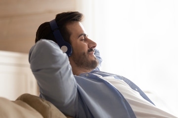 Calm young man relax on couch enjoying music in headphones