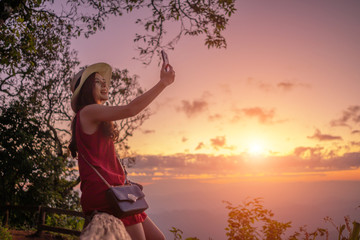 Smiling woman traveler in mountains at sunset and enjoying view of nature chiangmai landmark in thailand holding smartphone with backpack in holiday, relaxation concept, travel concept