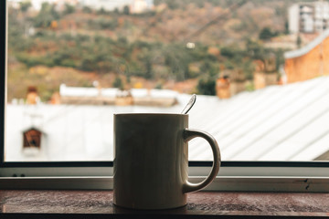 White mug of hot coffee on the edge of windows.