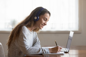 Smiling young woman in earphones studying on laptop