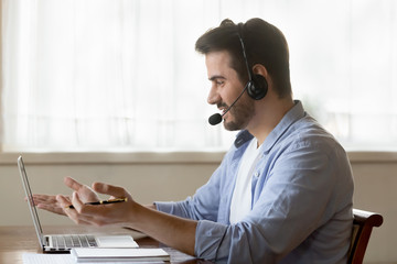 Male worker in headset consult clients on laptop online