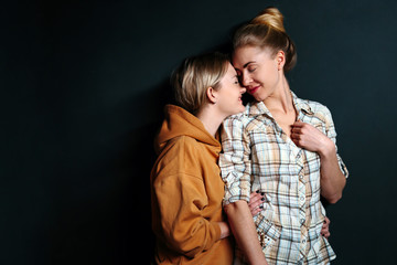 Portrait of young gay couple, lesbian women hugging on black background with copy space. Concept of love, family, gay marriage and pride
