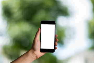 Mockup image of hand holding white mobile phone with blank white green nature background.