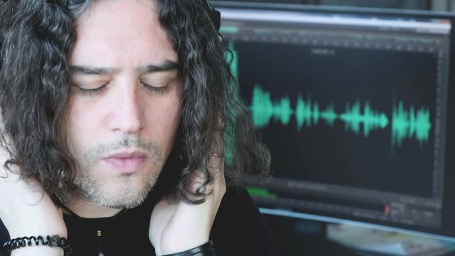 music composer man with long hair listen with headphones focusing with audio software histogram in pc screen background