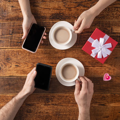 Valentine's Day celebration concept. A nice gift for your loved one. Hands of man and woman with coffee mugs on a wooden table background. Copy space. Flat lay. Close-up.
