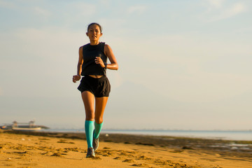 outdoors fitness portrait of young attractive and athletic Asian Indonesian woman in compression socks jogging on the beach doing running workout training hard