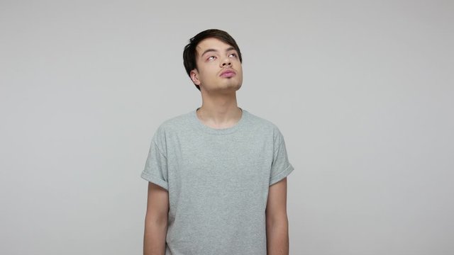 Let's think up plan! Pensive young brunette man in T-shirt looking inspired, pondering interesting creative idea, contemplating problem solution. indoor studio shot isolated on gray background