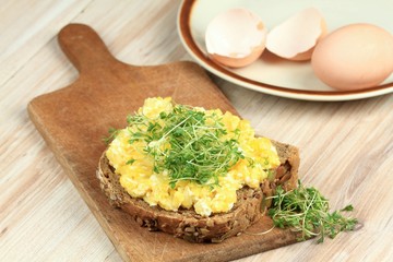 Scrambled eggs  over brown bread with garden cress. Homemade scrambled eggs served on the cutting...
