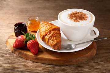 cup of cappuccino coffee, jam, strawberries and croissant