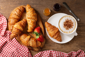 cup of cappuccino coffee, jam, strawberries and croissant, top view