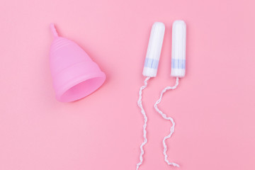 Pink reusable silicone menstrual cup and tampons on pink background. Top view. Concept of feminine hygiene, gynecology and health