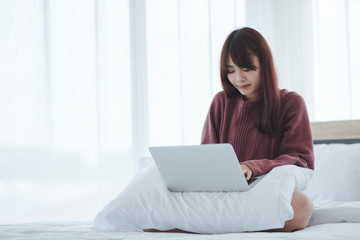 woman working on a laptop sitting on the bed in the house.