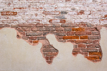 View of a house wall, which was built of red brick. The plaster has flaked off.