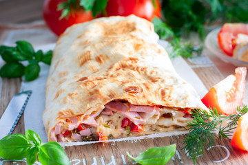 Baked pita roll with sausage and vegetables on a wooden board, selective focus