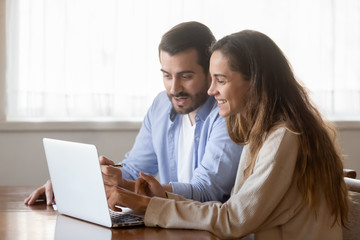 Smiling young couple sit at table using laptop together