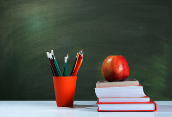 Back to school, orange pencil holder, stack of books on white table with red apple, empty green school board background, education concept. - Powered by Adobe