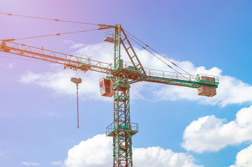Tower crane on a background of blue sky with clouds, colorful light of the sun