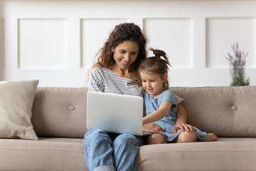 Fototapeta premium Smiling young mother teaching little daughter using computer applications.