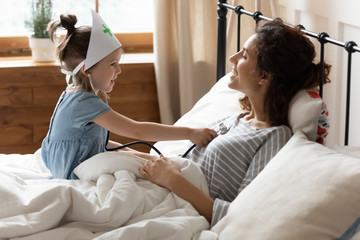 Small preschool girl playing doctor patient with smiling mother.