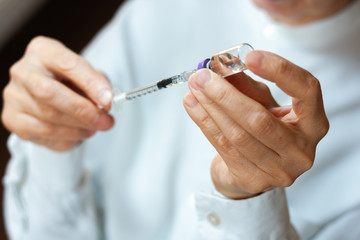 doctor in a white surgical gown and mask holds in hands a medical syringe and bottle with insulin for diabetes. Sugar addiction, insulin resistance, diabetes protection medical concept.