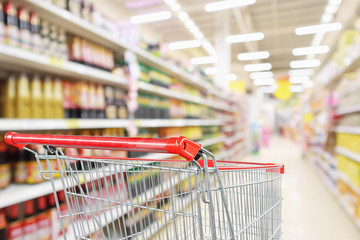 Empty shopping cart with abstract blur supermarket discount store aisle and product shelves...