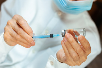 doctor in a white surgical gown and blue mask holds in hands a medical syringe and bottle with medicine for injection. Insulin resistance, diabetes protection health care medical concept.