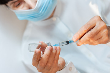 doctor in a white surgical gown and blue mask holds in hands a medical syringe and bottle with medicine for injection. Insulin resistance, diabetes protection health care medical concept.