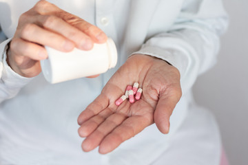 Female hand close up holding a medicine, elderly woman hands with pill on spilling pills out of bottle .