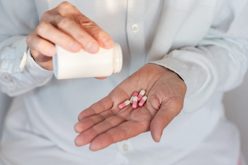Female hand close up holding a medicine, elderly woman hands with pill on spilling pills out of bottle .