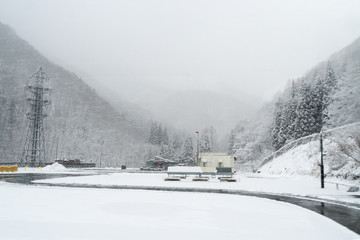 Blurred of view winter white snow in Pine tree forest beside road while vehicle drive across beautiful winter mountains nature blue sky in Japan. Cold season in snowing in tourism travel landscape