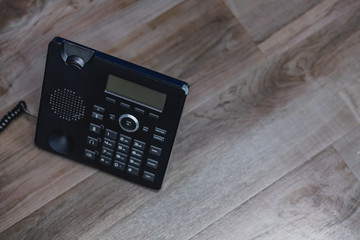 Close Up Black ip phone is placed on a wooden floor in the office.