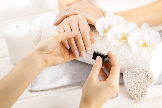 beautiful french manicure with orchid, candle and towel on the white wooden table. manicurist hands