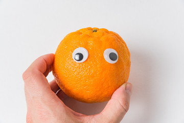 Food with Funny Faces. Mandarin with eyes. Hand holding tangerine character on white background
