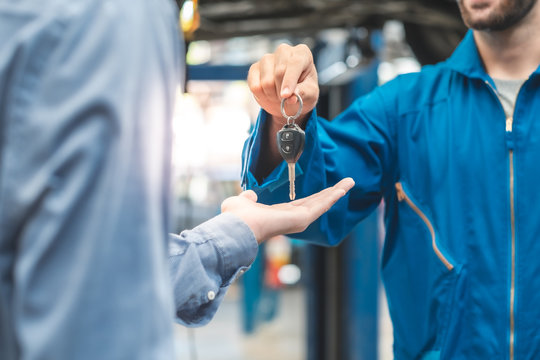  auto service. Handsome young auto mechanic in uniform is returning car key to a client, both are smiling.Customer giving him car keys to mechanic in service