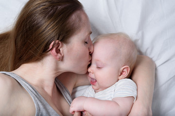 Happy mum holding infant child on hands. Beautiful young mother kissing her baby.