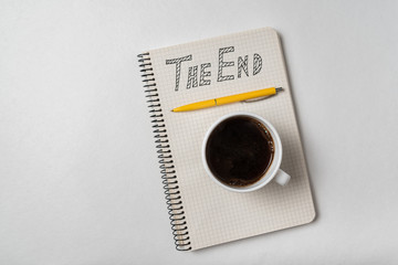 Copybook with The End text. Notepad, pen and cup of coffee on white background