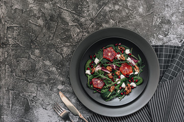 Top view plate of salad with blood oranges, greenery, goat cheese, pomegranate seeds and walnut on concrete gray background. Flat lay, copy spase