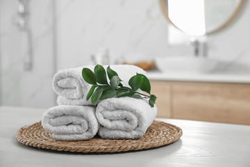 Rolled fresh towels and green leaves on white table in bathroom - obrazy, fototapety, plakaty