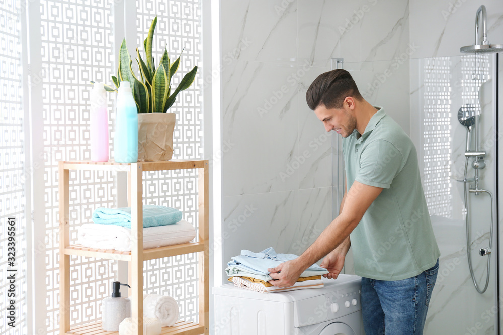 Sticker Happy man with clean clothes near washing machine in bathroom. Laundry day