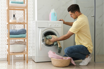Man putting clothes into washing machine in bathroom. Laundry day