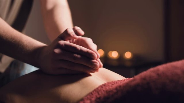 Close-up Young male massage therapist does back massage to a woman with a tattoo in a massage room with dim lights on the background of candles. Low key premium massage concept