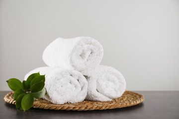 Fototapeta na wymiar Clean rolled bath towels, green branch and wicker mat on dark grey table