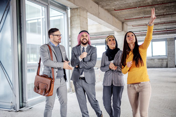 Obraz premium Two arab foreign investors standing in building in construction process and listening to real estate agent who is trying to convince them to buy it.