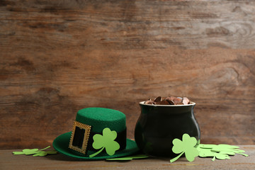 Pot of gold coins, hat and clover leaves on wooden table, space for text. St. Patrick's Day...